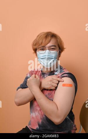 Junger asiatischer Mann zeigt seinen Arm, nachdem er eine Immunitätsimpfung erhalten hat. Stockfoto