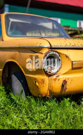 Altes gelbes Wrackauto im Vintage-Stil. Verlassene rostige gelbe Auto. Nahaufnahme der Scheinwerfer der Vorderansicht eines rostigen, gebrochenen, verlassenen Autos nea Stockfoto