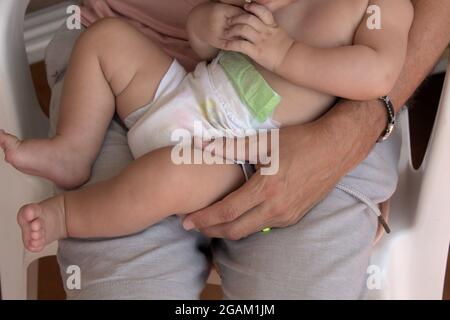 Im Vordergrund der Vater hält sein Baby mit Sorgfalt auf seinem Schoß Stockfoto