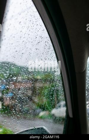 Regentropfen auf dem Fenstertürglas des Autos während der Regenzeit des Monsuns. Selektiver Fokus mit Bokeh-Hintergrund verwendet. Stockfoto