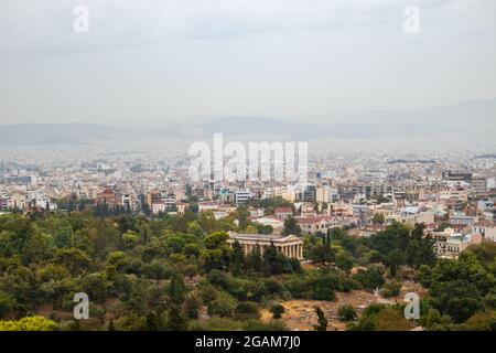 Blick auf den Tempel des Hephaestus im Grünen und das antike Stadtzentrum von Athen mit weißen Gebäuden an einem grauen nebligen Tag vom Areopagus-Hügel in der Nähe der Akropolis Stockfoto