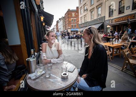 Zwei junge Frauen, die den „Tag der Freiheit“ feiern, der über ein Jahr der COVID-19-Sperrbeschränkungen endet in England, wo Menschen auf Tischen außerhalb der Stadt trinken Stockfoto