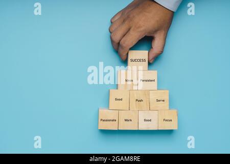 Hand des professionellen Geschäftsmann setzen Holzblock Schritt zum Erfolg auf weichem blauen Hintergrund, Idee und wie man Leistungskonzept zu bekommen Stockfoto