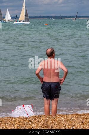 Älterer Mann, der kaltes Wasser schwimmt, oder wilder Schwimmer, der am Kiesstrand von cowes auf der Insel wight während der jährlichen cowes Week Regatta ist. Stockfoto