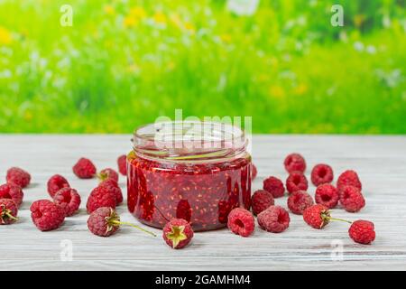 Marmelade und Himbeeren auf einem hellen Holztisch vor dem Hintergrund eines grünen Rasens Stockfoto