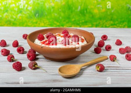 Frisches Frühstück – Haferflocken mit Himbeeren auf einem Holztisch vor dem Hintergrund eines grünen Rasens Stockfoto