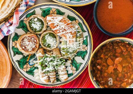 Tacos dorados mit Huhn und Sopes mit roter und grüner Sauce, Frijoles Charros, würzige rote Sauce, traditionelle mexikanische Küche Stockfoto