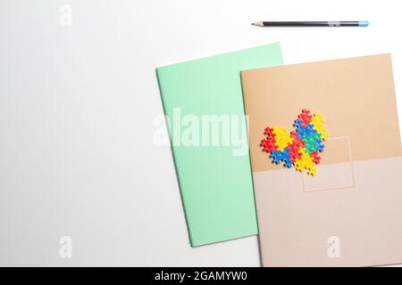Bunte Notizbücher und Herz aus Kunststoff-Konstruktions-Puzzleteilen auf weißem Hintergrund Stockfoto