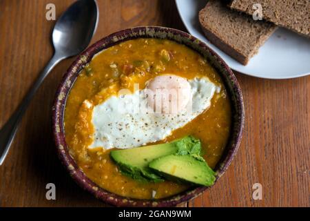 Indische Suppe mit Spiegelei und Avocado serviert mit Roggenbrot. Stockfoto