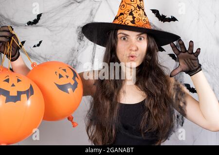 Eine Frau in einem Hexenkostüm mit Hut und Handschuhen im Hintergrund mit Fledermäusen hält Kürbiskugeln und sagt boo. Halloween-Leute Stockfoto