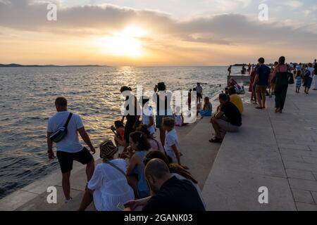 ZADAR, KROATIEN - 21. Jul 2021: Nahaufnahme vieler Menschen, die den Sonnenuntergang am Meer in Kroatien beobachten Stockfoto