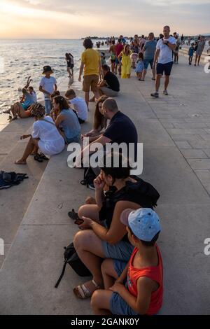 ZADAR, KROATIEN - 21. Jul 2021: Eine vertikale Aufnahme von vielen Menschen, die den Sonnenuntergang am Meer in Kroatien beobachten Stockfoto