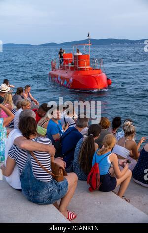 ZADAR, KROATIEN - 21. Jul 2021: Eine vertikale Aufnahme von Menschen, die am Abend in Zadar, Kroatien, ein rot ankommendes Taxiboot beobachten Stockfoto