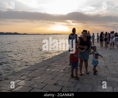 ZADAR, KROATIEN - 21. Jul 2021: Nahaufnahme vieler Menschen, die den Sonnenuntergang am Meer in Kroatien beobachten Stockfoto