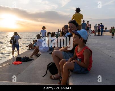 ZADAR, KROATIEN - 21. Jul 2021: Nahaufnahme vieler Menschen, die den Sonnenuntergang am Meer in Kroatien beobachten Stockfoto