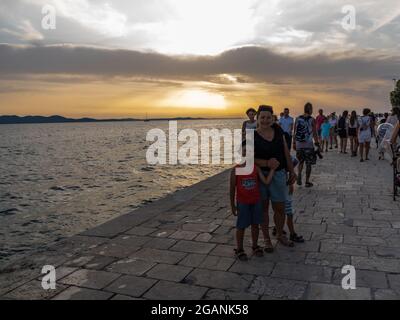 ZADAR, KROATIEN - 21. Jul 2021: Nahaufnahme vieler Menschen, die den Sonnenuntergang am Meer in Kroatien beobachten Stockfoto