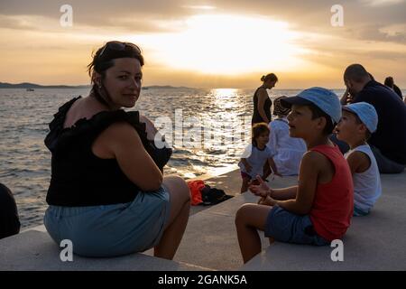 ZADAR, KROATIEN - 21. Jul 2021: Nahaufnahme vieler Menschen, die den Sonnenuntergang am Meer in Kroatien beobachten Stockfoto