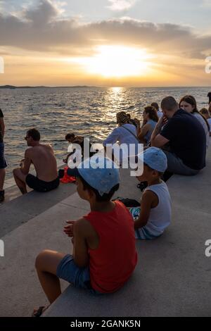 ZADAR, KROATIEN - 21. Jul 2021: Eine vertikale Aufnahme von vielen Menschen, die den Sonnenuntergang am Meer in Kroatien beobachten Stockfoto