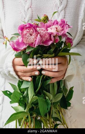 Kurze junge Frau in weißem Strickpullover mit einem Bouquet aus frischen Blumen rosa Pfingstrosen. Stockfoto