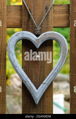 Graues Holzherz, das an einem hölzernen Pfostenzaun in einem Garten hängt. Stockfoto