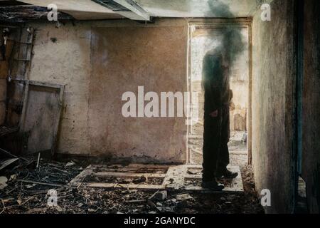 Ein Horrorkonzept. Von einer Figur ohne Gesicht, die in der Tür eines verfallenden Zimmers in einem verlassenen zerstörten Haus steht Stockfoto