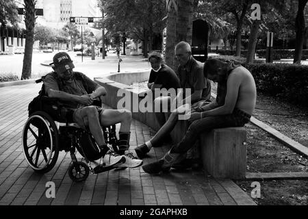 Tampa, Florida, USA. Juli 2021. Obdachlose Männer und Frauen vergehen die Zeit im Schatten der Bäume entlang einer Straße in der Innenstadt von Tampa. Die wenigen Unterstände der Stadt seien voll, sagten Befürworter. „Wir bekommen viele Obdachlose, die mit einer Fahrkarte für den Bus aus anderen Städten hierher kommen“, bemerkte ein örtlicher Polizeibeamter. „viele von denen, die auf der Straße schlafen, haben Probleme mit psychischen Erkrankungen“, sagte er. (Bild: © Robin Rayne/ZUMA Press Wire) Stockfoto