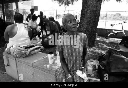 Tampa, Florida, USA. Juli 2021. Obdachlose Männer und Frauen vergehen die Zeit im Schatten der Bäume entlang einer Straße in der Innenstadt von Tampa. Die wenigen Unterstände der Stadt seien voll, sagten Befürworter. „Wir bekommen viele Obdachlose, die mit einer Fahrkarte für den Bus aus anderen Städten hierher kommen“, bemerkte ein örtlicher Polizeibeamter. „viele von denen, die auf der Straße schlafen, haben Probleme mit psychischen Erkrankungen“, sagte er. (Bild: © Robin Rayne/ZUMA Press Wire) Stockfoto