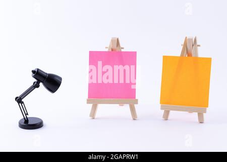 Zwei hölzerne Easels Miniature mit blanker quadratischer Leinwand oder Memopapier - Mockup. Mini-Holzständer mit sauberer Tafel und kleiner schwarzer Tischleuchte auf weißem Hintergrund, Kopierraum Stockfoto