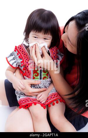 Asiatische Mutter wischt snot sie Tochter. Kleines Mädchen mit Allergiesymptom und sitzt auf dem Schoß einer jungen Frau. Auf weißem Hintergrund Stockfoto