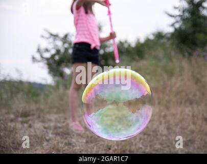 Ein kleines Mädchen in der Natur spielt mit großen Seifenblasen. Stockfoto