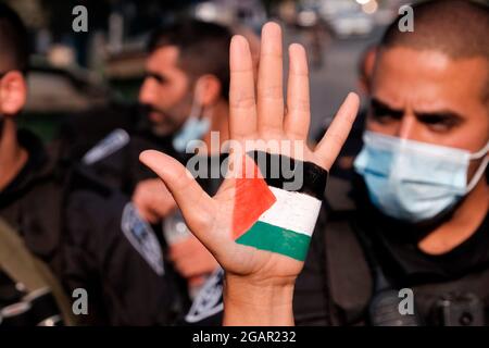 Eine mit den Farben der palästinensischen Flagge gemalte Demonstratorin hebt ihre Hand vor der israelischen Polizei während einer Demonstration gegen die israelische Besatzung und Siedlungsaktivitäten in Scheich Jarrah, einem überwiegend palästinensischen Viertel, am 30. Juli 2021 in Ostjerusalem, Israel. Das palästinensische Viertel Sheikh Jarrah ist derzeit das Zentrum einer Reihe von Eigentumsstreitigkeiten zwischen Palästinensern und rechtsgerichteten jüdischen Israelis. Einige Häuser wurden nach einem Gerichtsurteil von israelischen Siedlern besetzt. Stockfoto