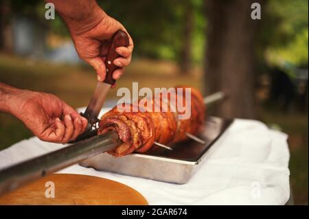 Zugeschnittenes Foto von Menschenhänden, die Schweinefleisch auf dem Spieß schneiden Stockfoto