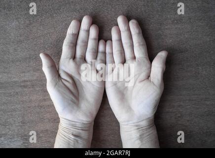 Blasse Palmaroberfläche beider Hände. Blutarme Hände einer asiatischen, chinesischen Frau. Isoliert auf Holzhintergrund. Stockfoto