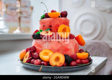 Mehrschichtiger Kuchen aus Beeren und Früchten. Frischer Obst- und Beerensalat in Form eines Kuchens, der mit Minzblättern verziert ist. Sommerdessert und Vitaminkonz Stockfoto