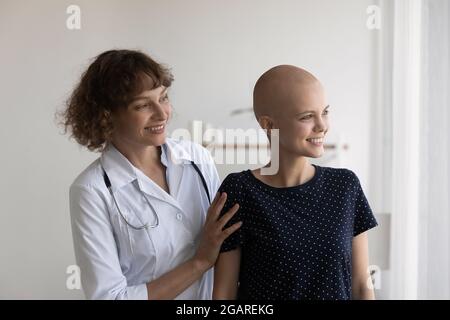 Mitfühlender junger Onkologe, der lächelnde Patienten in Innenräumen unterstützt. Stockfoto