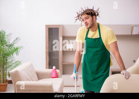 Junger männlicher Auftragnehmer, der auf dem Kopf einen stacheligen Kranz trägt und Hausarbeit leistet Stockfoto