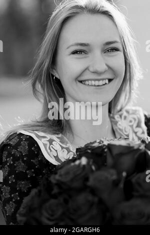 Lächelnde junge kaukasische Braut, leichtes Kleid posiert. Brautstrauß in ihren Händen. Schwarzweiß-Foto. Stockfoto