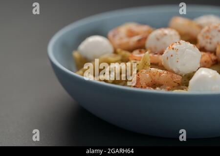 Penne-Pasta mit Garnelen und Mozzarella und Pesto in blauer Schale mit Kopierfläche, flacher Fokus Stockfoto