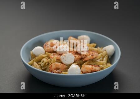 Penne mit Garnelen und Mozzarella und Pesto in blauer Schale, flacher Fokus Stockfoto