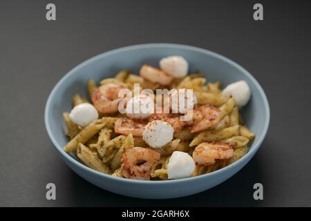 Penne mit Garnelen und Mozzarella und Pesto in blauer Schale, flacher Fokus Stockfoto