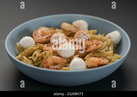 Penne mit Garnelen und Mozzarella und Pesto in blauer Schale, flacher Fokus Stockfoto