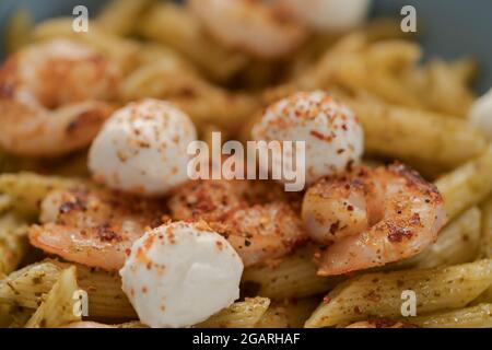 Penne mit Garnelen und Mozzarella und Pesto in blauer Schale, flacher Fokus Stockfoto