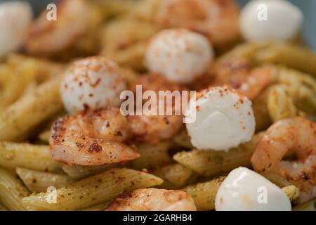 Penne mit Garnelen und Mozzarella und Pesto in blauer Schale, flacher Fokus Stockfoto