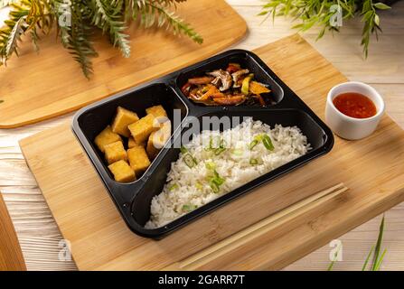 Reis mit Tofu und Gemüseeintopf in der Take-Out-Box auf Bambus-Schneidebrett Stockfoto