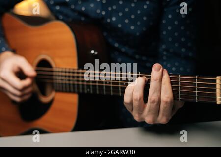 Nahaufnahme des unverkennbaren Gitarristen, der am Schreibtisch im dunklen Wohnzimmer akustische Gitarre spielt, selektiver Fokus. Stockfoto