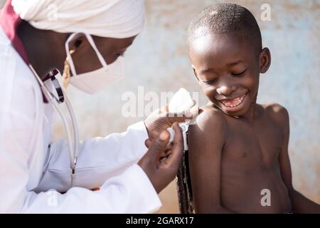 Nahaufnahme eines kleinen afrikanischen Jungen mit seiner Zunge zwischen den Zähnen, halb beängstigend, halb amüsiert über einen Tropfen Flüssigkeit aus der Spritze kommen, während sein Stockfoto