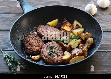 Fleischschnitzel mit Bratkartoffeln und Rosmarin in einer Pfanne auf einem Holztisch Stockfoto
