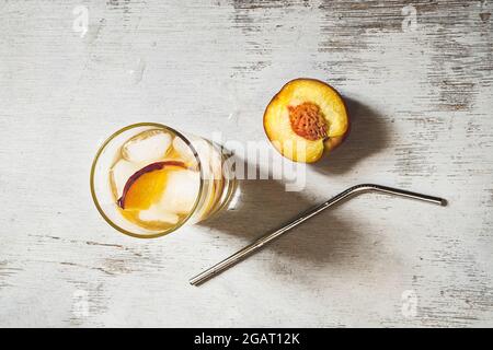 Pfirsich-Erfrischungsgetränk mit Eis, einer Hälfte frischem Pfirsich und Metallstroh für Getränke auf einem alten weißen Holztisch, Draufsicht Stockfoto