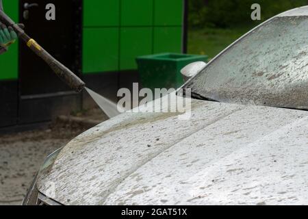 Autowäsche. Das Auto wird unter dem Druck eines Wasserstrahls gewaschen. Mit einem Wasserspray Schmutz von der Fahrzeugoberfläche abwaschen. Stockfoto