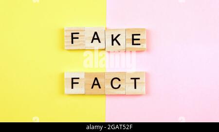 Ein Spielstein aus Wortbildung und Fälschung auf einem gelben und rosa Hintergrund. Selektiver Fokus auf das Wort Fake und Fact. Stockfoto
